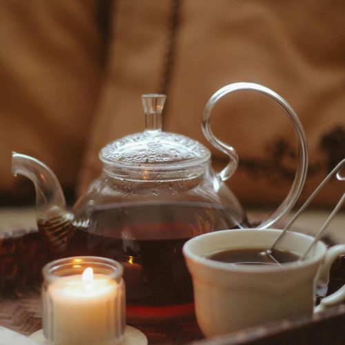 Elegant glass teapot with tea cup and candle, creating a warm, inviting atmosphere.